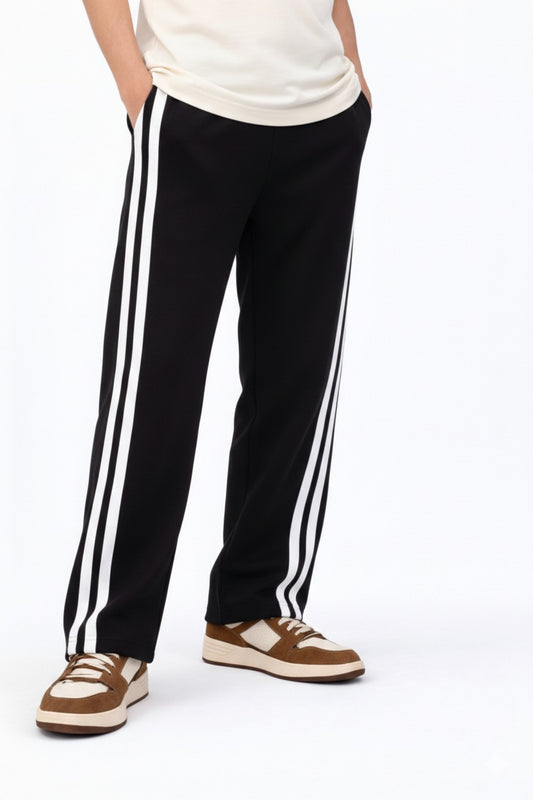 Black track pants with white stripes worn by a person on a white background